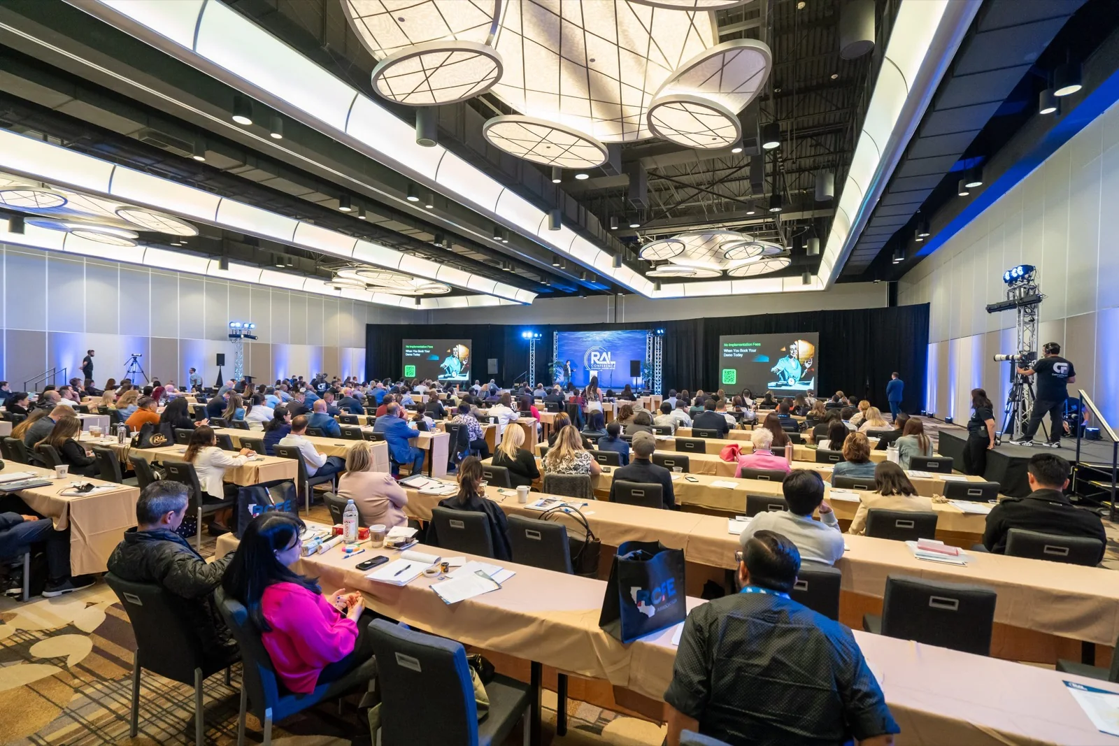 A conference breakout room, filmed wide, running concurrently with the main general session
