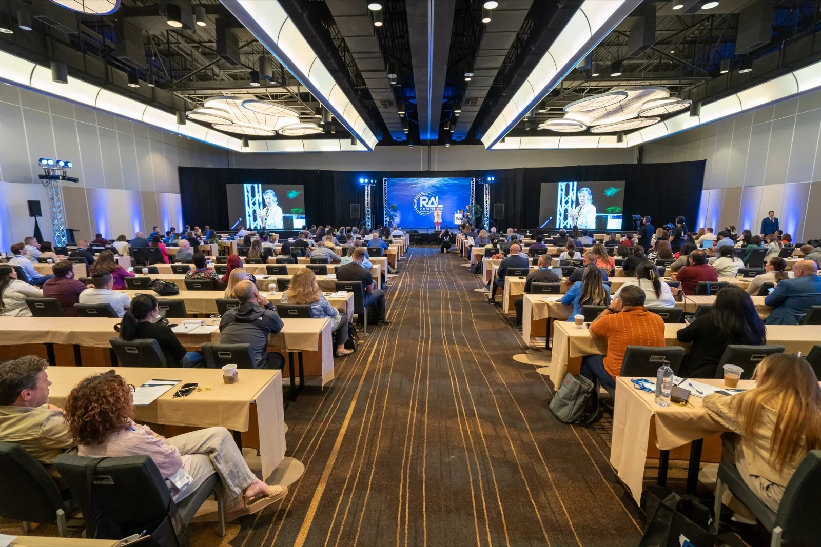 A conference general session with IMAG screens flanking the stage