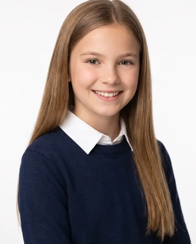 Young actor headshot of a girl with long light-brown hair in a navy sweater with a white collar on a white backdrop