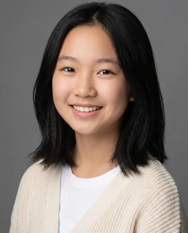 Young actor headshot of a teenage girl with a black bob in a cream cardigan on a grey backdrop