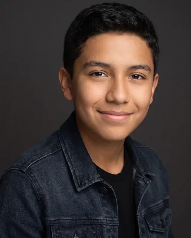 Young actor headshot of a teenage boy in a denim jacket on a dark backdrop