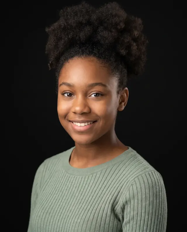 Young actor headshot of a teenage girl in a sage-green sweater on a black backdrop