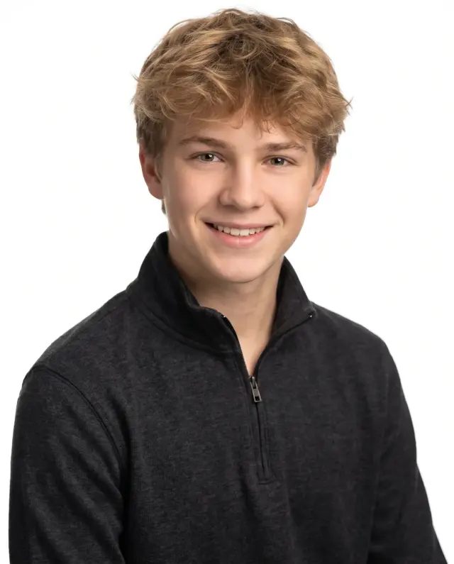 Young actor headshot of a teenage boy with curly blond hair in a black quarter-zip on a white backdrop