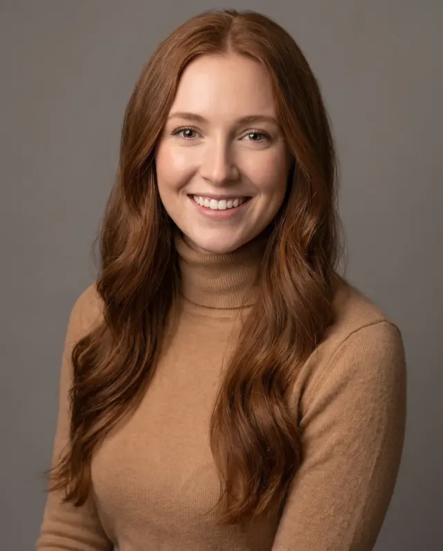 Actor headshot of a woman with long auburn hair in a camel turtleneck on a grey backdrop