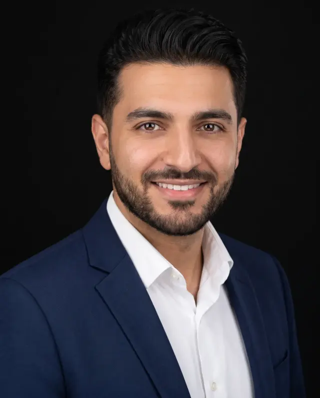 Professional headshot of a bearded man in a navy blazer and white shirt on a black backdrop