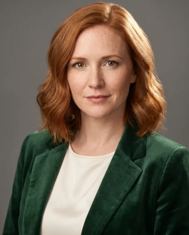 Actor headshot of a red-haired woman in a green velvet blazer on a grey backdrop