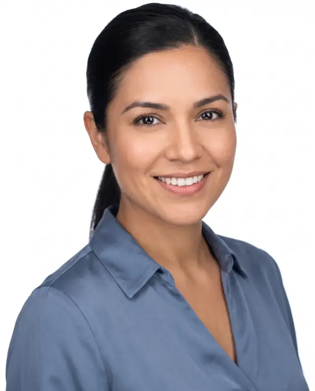 Professional headshot of a woman with a sleek ponytail in a blue satin blouse on a white backdrop