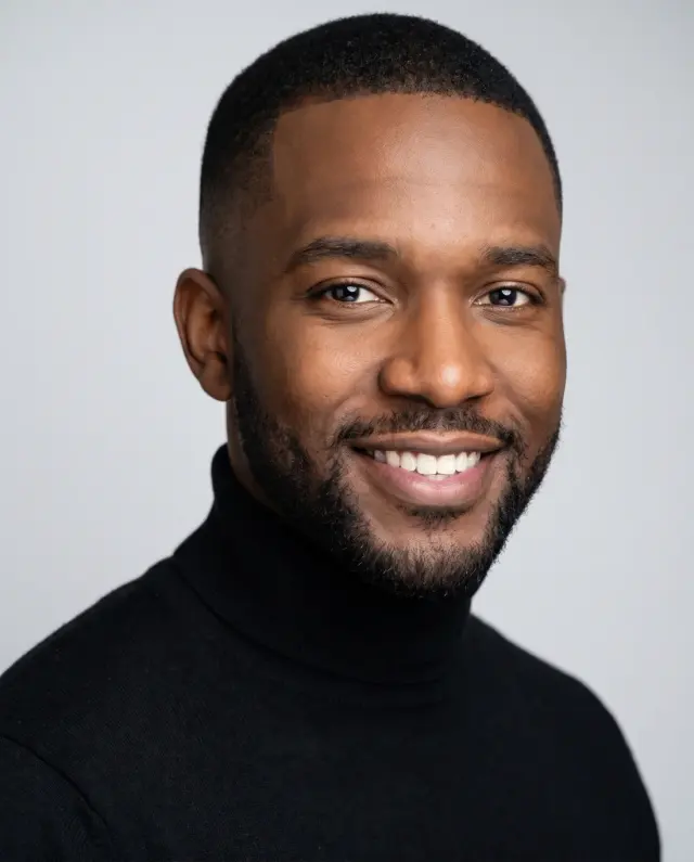 Actor headshot of a bearded man in a black turtleneck on a light grey backdrop