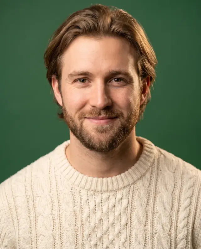 Actor headshot of a bearded man in a cream cable-knit sweater on a green backdrop