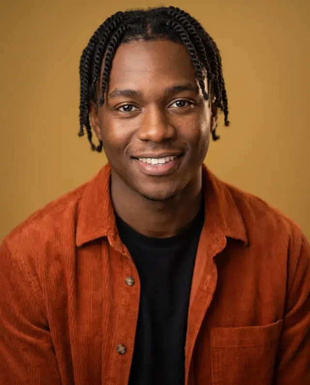 Actor headshot of a young man with twists in a rust corduroy shirt on a mustard backdrop