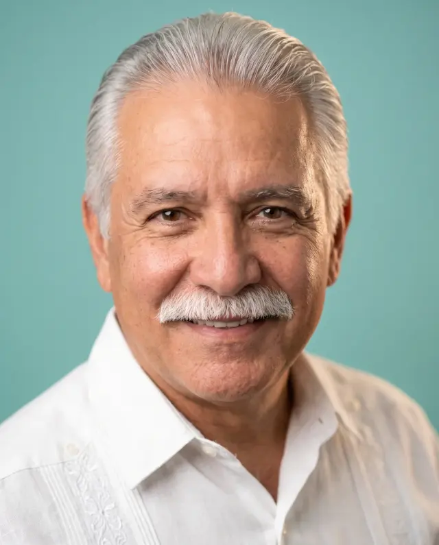 Headshot of an older man with white hair and a moustache in a white shirt on a teal backdrop