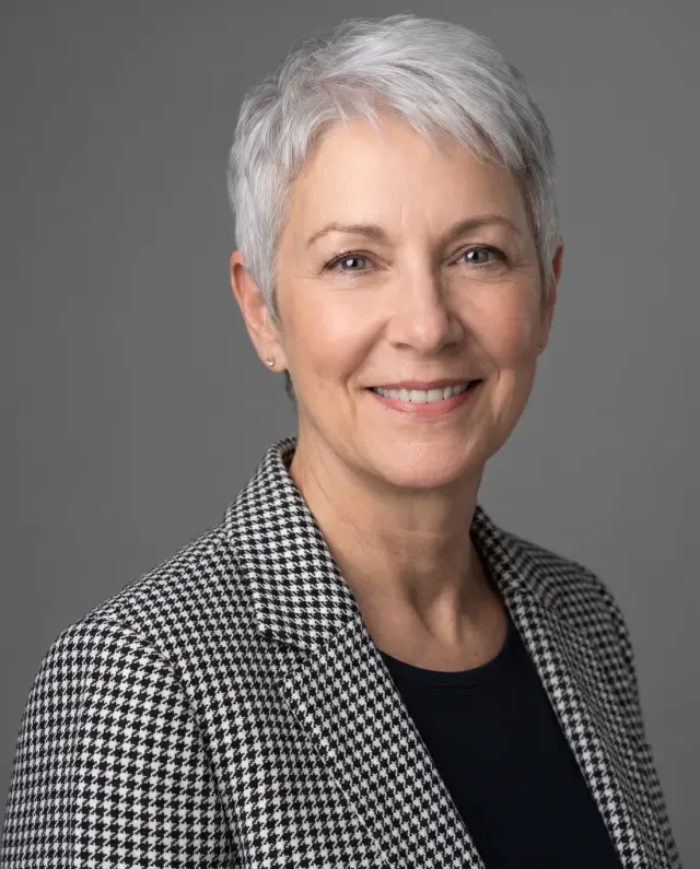 Executive headshot of a woman with short silver hair in a houndstooth jacket on a grey backdrop