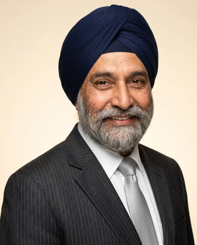 Executive headshot of a man in a navy turban and pinstripe suit on a cream backdrop