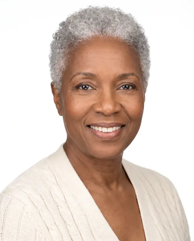 Headshot of an older woman with short grey curls in a cream cardigan on a white backdrop