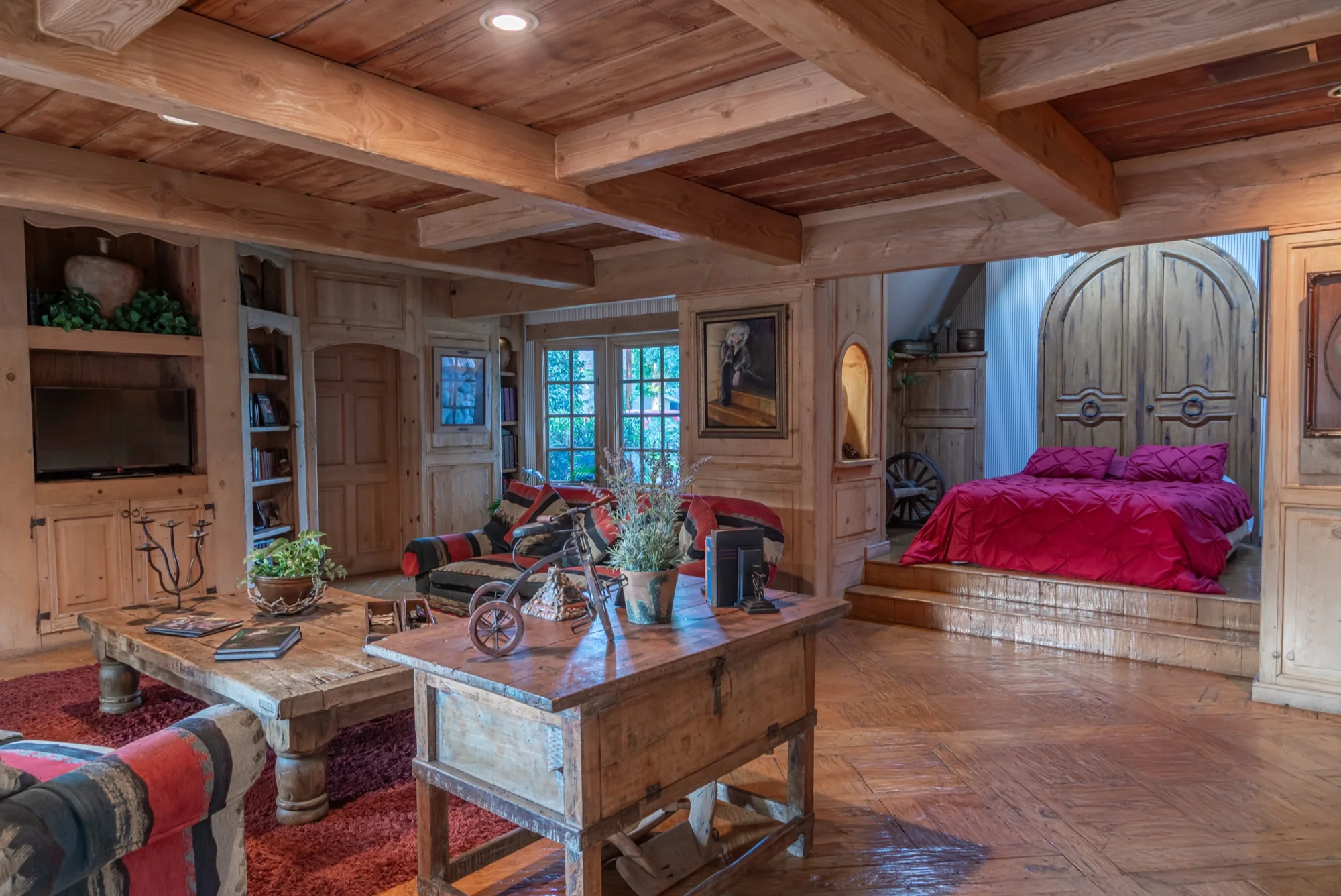 A beamed room with an arched door and a red bed at The Enchanted Manor
