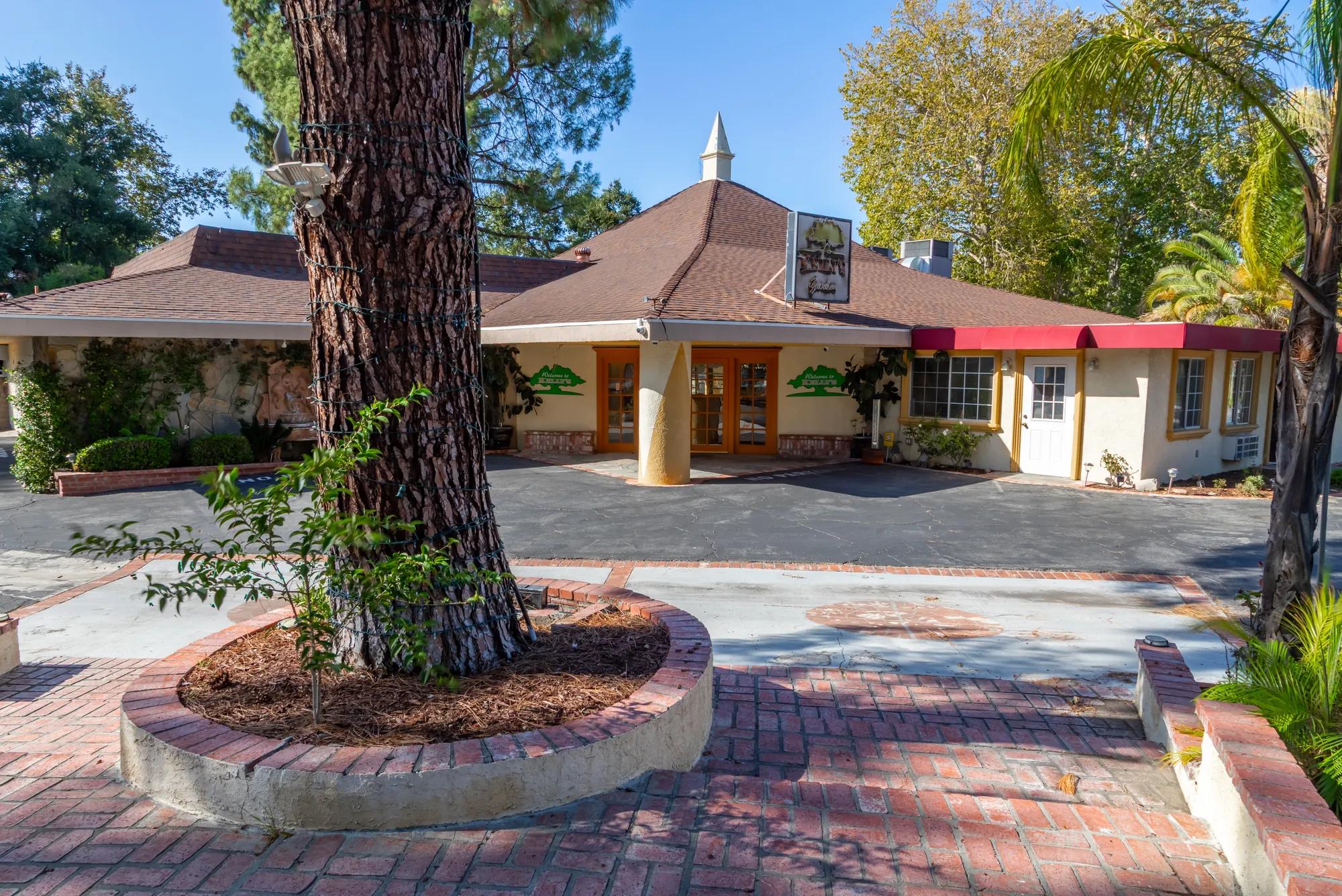 The banquet building under tall pines with its red awnings at Kelly's Wedding Garden