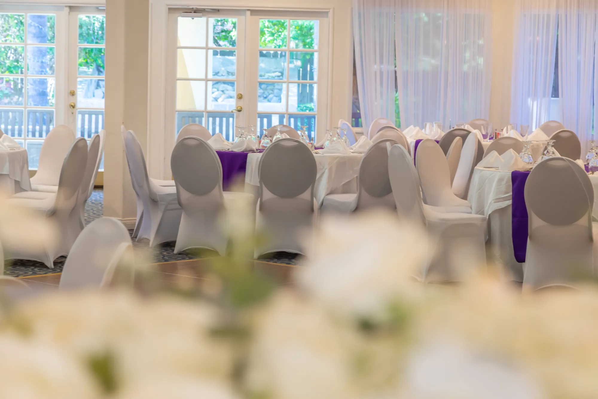 White roses in the foreground with the French doors and set tables behind at Kelly's Wedding Garden