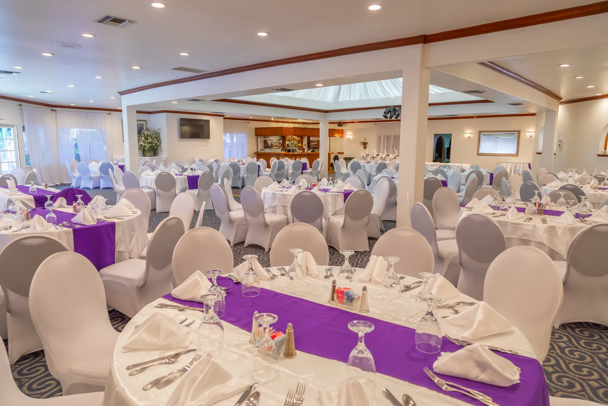 Round tables dressed in white and purple in the banquet room at Kelly's Wedding Garden