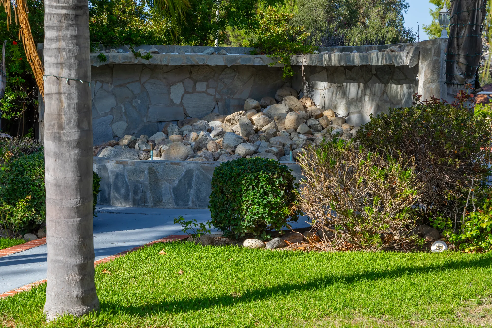 A palm trunk in front of the stone waterfall wall at Kelly's Wedding Garden